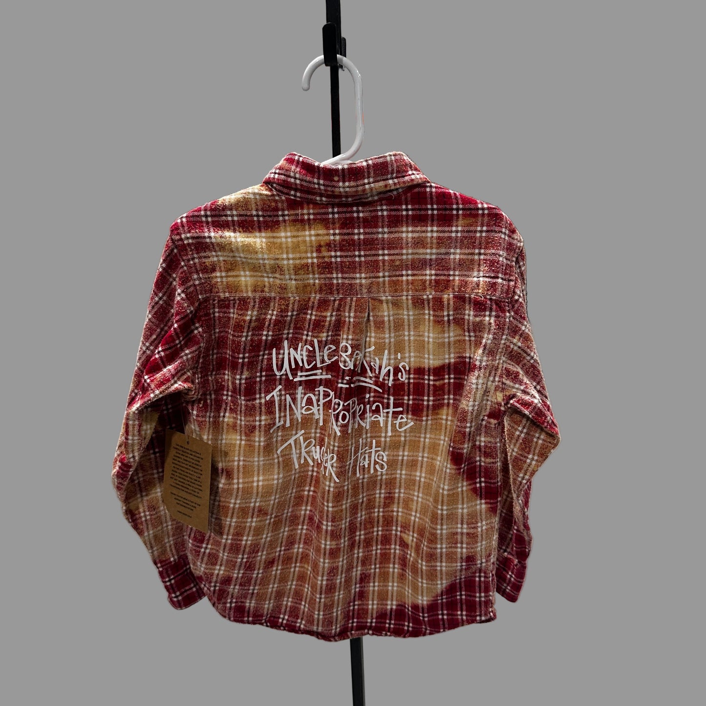 Plaid shirt with text on a hanger against a white wall with various items in the background.