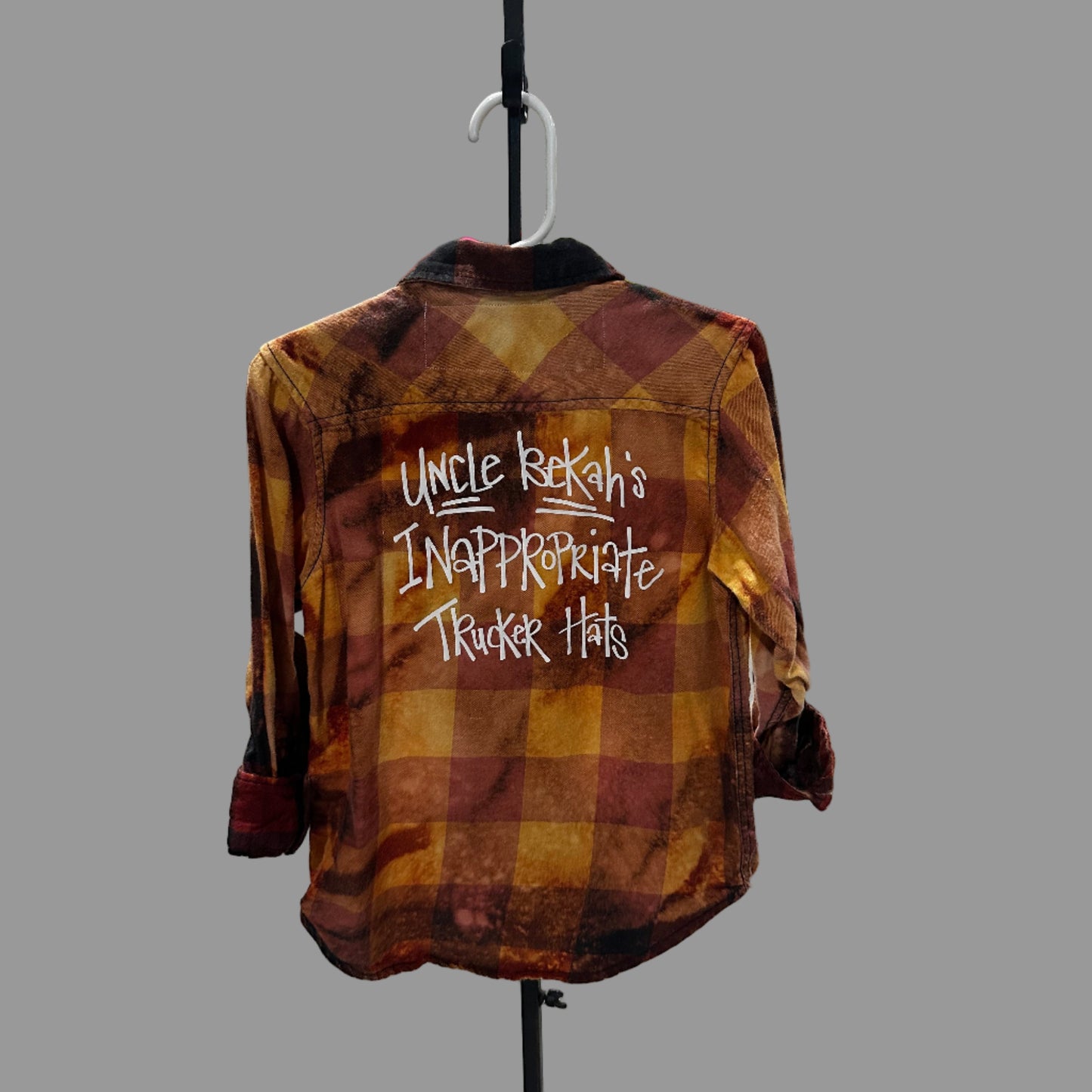 Plaid shirt with text on a stand against a white wall with shelves.